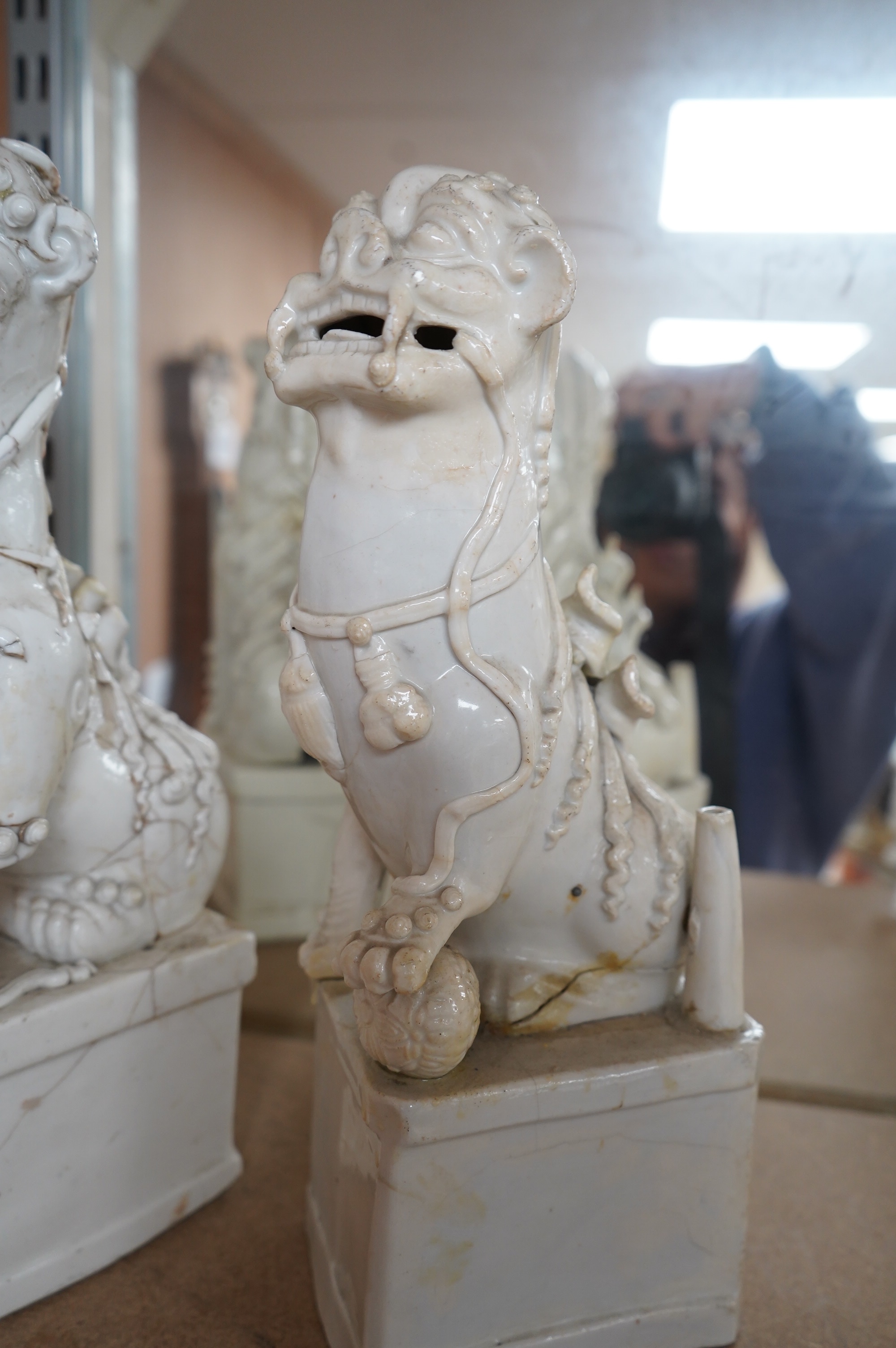 Two large Chinese Dehua blanc de chine Buddhist lion joss-stick holders, Kangxi period, each seated, one paw raised on a ball, on rectangular pedestal basis, 35cm high, Condition - extensive cracks or repairs